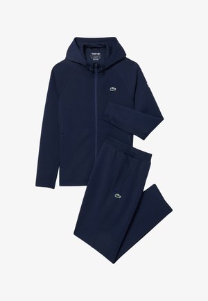 Marineblauwe hoodie met rits en bijpassende joggingbroek met groen krokodillenlogo op borst en dij, plat liggend op een witte achtergrond.