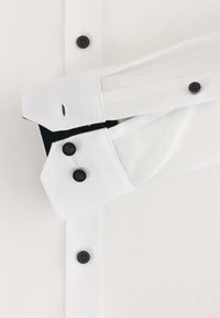 Weißes Hemd mit Knöpfen in Schwarz; bietet einen strukturierten Stoff, einen spitzen Kragen und umgeschlagene Manschetten mit schwarzem Futter.