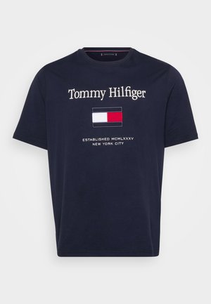 T-shirt in cotone blu navy con il logo "Tommy Hilfiger" ricamato in bianco, accompagnato da un piccolo emblema del logo in rosso, bianco e blu sotto.