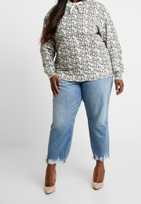 Mikina s kapucí v černo-bílé hadí potisku, kombinovaná s modrými roztrhanými džíny a tělovými vysokými podpatky. Neformální design outfitu.