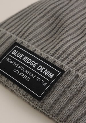 Szara dzianinowa czapka z prążkowanym wzorem. Posiada czarną metkę z białym napisem "BLUE RIDGE DENIM" oraz hasłem poniżej.