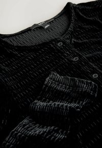 Zwarte, gestructureerde longsleeve shirt van zacht materiaal, met een ronde halslijn en een placket met drie knopen.