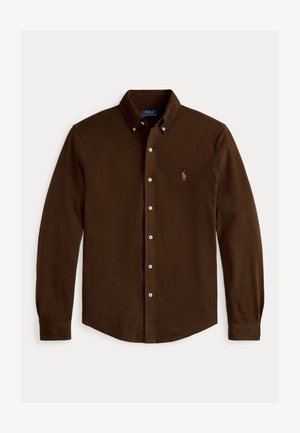 Brūna krekla ar garām piedurknēm un pogām, izgatavota no kokvilnas. Iezīmē klasisku apkakli un mazu izšūtu logo uz krūtīm. Pogājama piegriezuma dizains.