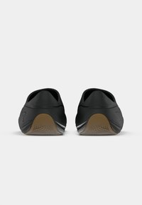 Czarne buty sportowe z gładką cholewką, zakrzywioną formą i gumowymi podeszwami. Tył posiada teksturowany wzór oraz akcent logo.