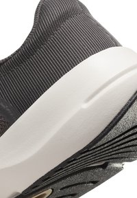 Close-up van een sportieve schoen met een gestructureerde grijze mesh bovenzijde, een witte tussenzool en een zwarte rubberen buitenzool met duidelijke groeven.