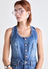 Dżinsowy kombinezon bez rękawów z dopasowaną górą, zapięciem na guziki i dwiema przednimi kieszeniami. Charakteryzuje się jasnoniebieskim odcieniem i miękką teksturą.