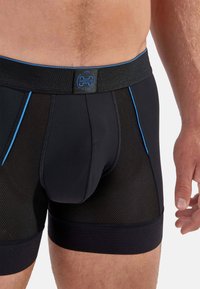 Schwarze Boxer-Shorts aus Mesh und Stoff mit einem blauen Streifen und Logo am Bund, gefertigt für Komfort und Atmungsaktivität.