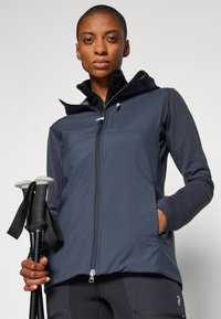 Mornarska kapuca z zadrgo, ki vključuje hibridno zasnovo iz materialov softshell in flis. Ima žepe na zadrgo in kontrastne rokave.