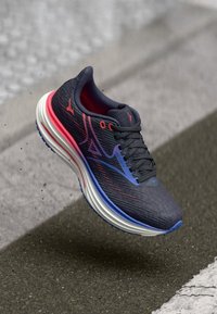 Skriešanas kurpes melnā krāsā ar rozā un zilu akcentu. Izgatavotas no teksturēta auduma, ar mīkstinātu zoli un auklu aizdari.