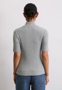 Dopasowany szary top prążkowany z półgolfem i krótkimi rękawami, zestawiony z dżinsami w kolorze niebieskim z wysokim stanem. Minimalistyczny design, gładka tekstura.