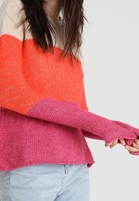Strickpullover mit einem Farbkombination-Design in Orange, Pink und Beige. Lange Ärmel mit Daumenlöchern, lockere Passform und weicher Textur.