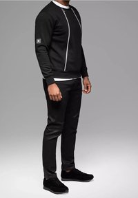 Sudadera negra con detalles de piping blancos, combinada con pantalones negros ajustados y zapatillas negras, mostrando un estilo atlético casual.