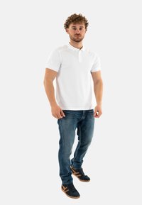 Polo bianco a maniche corte, jeans blu e sneakers nere con dettagli color beige. Design semplice e classico; senza pattern o loghi visibili.