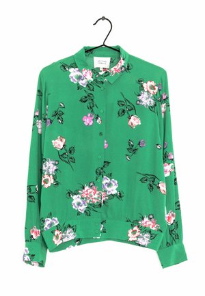 Blouse à manches longues vert avec un motif floral rouge, rose et violet. Boutonnage devant, col et ourlet légèrement incurvé.