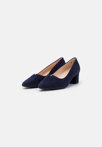 Zapatos de tacón azul marino de ante con punta afilada y pequeño tacón cuadrado, que presentan un sutil detalle de corte en el empeine y un forro interior suave.