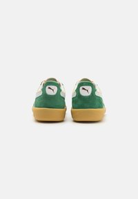 Un paio di sneakers verdi e bianche con suole in gomma, viste da dietro, con un logo Puma marrone sulla linguetta del tallone.