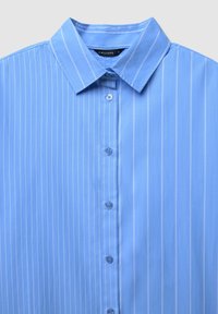 Chemise bleu clair à boutons avec des rayures blanches verticales, un col pointu et une texture lisse. Comprend six boutons sur le devant.