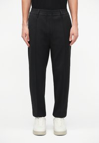 Pantaloni negri cu o croială relaxată, prevăzuți cu un talie elastică, închidere cu șnur și două pliuri frontale. Asociat cu adidași albi.