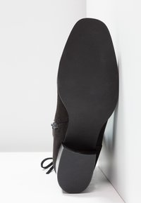 Bottine en daim noir avec un bout rond, une semelle en caoutchouc texturée et un petit talon empilé ; équipée de lacets et d'une fermeture éclair latérale.