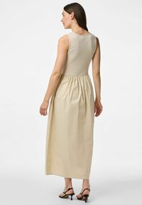 Bež haljina bez rukava s prilagođenim gornjim dijelim i raširenom, naboranom suknjom. Mekani materijal s glatkom teksturom i punom dužinom.