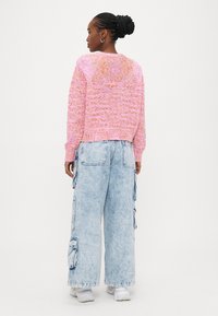 Rozā adīts džemperis ar reljefa rakstu, kombinēts ar gaiši ziliem, vaļīgiem cargo džinsiem ar sānu kabatām.