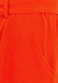 Oranžové lněné šortky s elastickým pasem, na kterém je nařasení, a postranními kapsami s texturovaným povrchem.