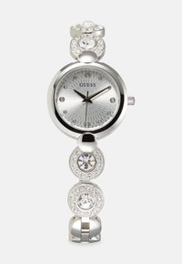 Orologio Guess argento con quadrante rotondo, motivo a raggi di sole e indici in cristallo. Il bracciale presenta anelli circolari con pietre trasparenti e dettagli.