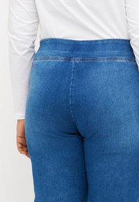 Jeans de mezclilla azul con una cintura alta, con una textura suave y costuras sutiles, que muestran un diseño ajustado desde la vista trasera.