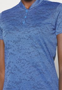 Polo bleu à surface texturée, présentant un motif subtil, manches courtes et trois boutons bleu clair au col.