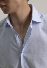 Camisa de vestir a cuadros azul claro con cuello puntiagudo, que cuenta con cierre de botones y una textura de tela suave.