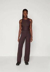 Tumši brūns divdaļīgs kostīms, kas sastāv no piegrieztas bezpiedurkņu blūzes un brīvām biksēm, izgatavots no mīksta auduma ar gludu tekstūru.