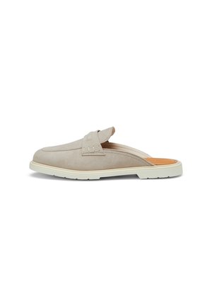 Beige slip-on mule-sko med hvid sål, lukket tå og en dekorativ rem tværs over toppen, vist fra siden på en hvid baggrund.