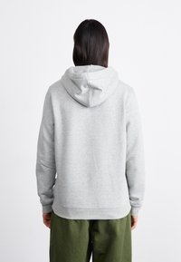 Grå bomulds hoodie med snorhætte og ribrækkede manchetter, set fra ryggen, parret med løse grønne bukser. Glat tekstur.