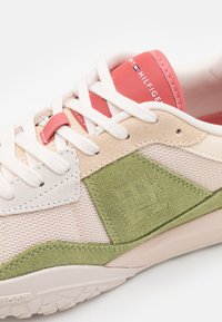 Beige a zelené semišové tenisky s bílými tkaničkami, červeným štítkem na jazyku a texturovanou síťovinou na boční straně, se subtilním embosovaným logem.
