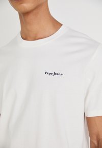Balta medvilninė marškinėliai su apvalia iškirpte ir trumpomis rankovėmis, ant kairiojo krūtinės yra mažas tamsiai mėlynas "Pepe Jeans" logotipas.