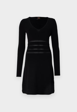 Črna dolga obleka z dolgimi rokavi in V-izrezom, ki se ponaša z teksturiranimi vodoravnimi pasovi in dekorativnimi perforacijami okoli pasu in roba.