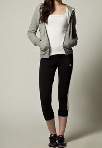 Felpa grigia con zip, canotta bianca, leggings neri a vita alta con righe bianche e scarpe da ginnastica nere, tutto progettato per l'abbigliamento sportivo.