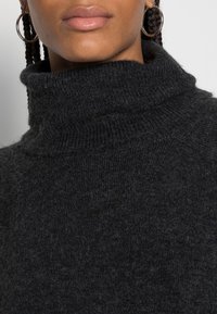 Maglione a collo alto di un grigio scuro realizzato in morbido materiale lavorato a maglia, con un collo alto e una finitura texture.