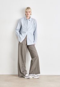 Camisa de botones azul claro con un diseño casual, combinada con pantalones de cuadro grises de pierna ancha y zapatillas grises. Look simple y limpio.