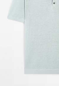 Světle modrá polokošile s krátkým rukávem, vyrobená z texturovaného pleteného materiálu, s dvouknoflíkovou légou a ribovanými manžetami.