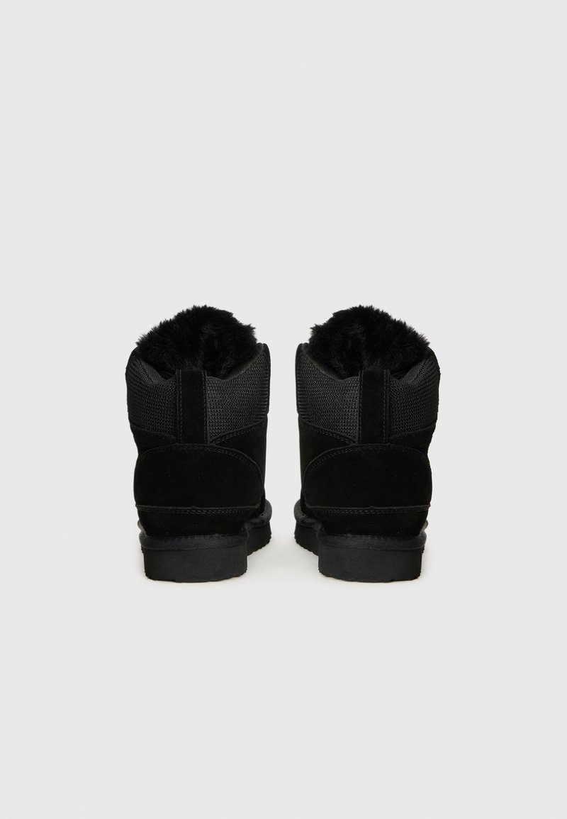 Bottines noires avec un dessus en suède et tissu texturé. Doublure intérieure en fourrure noire et semelle en caoutchouc épaisse. Design simple et arrondi.