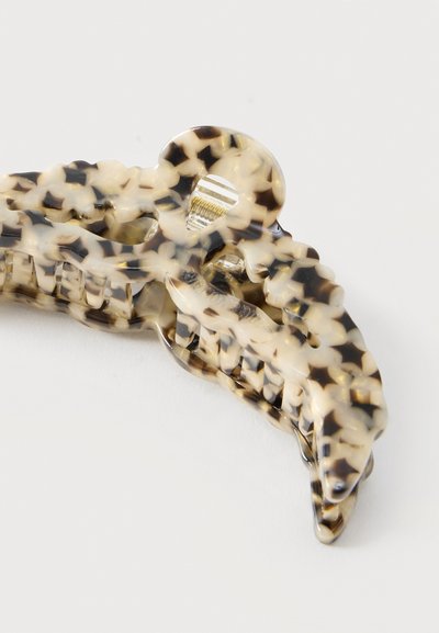 Pince à cheveux en plastique à motif écaille de tortue avec dents entrelacées et mécanisme à ressort en métal sur fond blanc.