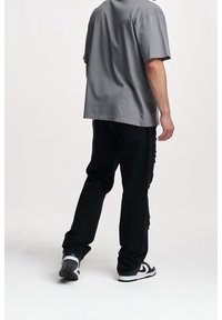 Šedé bavlněné tričko s volným střihem, spárované s potrhanými černými džíny a černo-bílými teniskami, pohled zezadu.