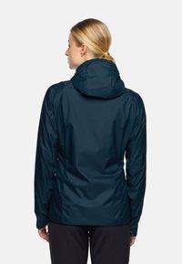 Veste imperméable bleu marine avec capuche, poignets élastiques et texture lisse. Le design comprend des coutures prononcées et une silhouette ajustée.