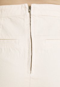 Valkoiset vetoketjuhousut, joissa on YKK-metallivetoketju, kaksi etutaskua ja sileä kangasrunko.