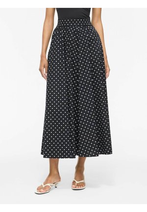 Gonna midi nera con pois bianchi, indossata con sandali beige con tacco e un top nero, mostrata dalla vita ai piedi.