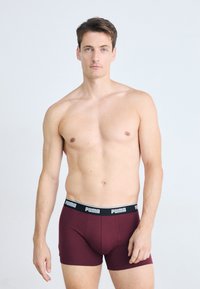 Boxeri burgundy cu un brâu elastic negru, având logo-ul "PUMA" în alb. Material moale, design ajustat, lungime până la mijlocul coapsei.