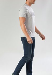 Camiseta gris de manga corta con texto negro, combinada con jeans de mezclilla azul. La tela parece suave, con un diseño ajustado y un aspecto casual.