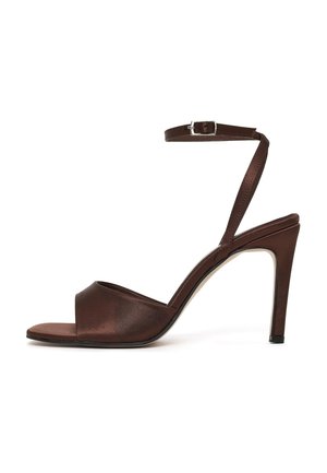 Sandale à talon haut marron avec bout ouvert, fine bride à la cheville avec boucle argentée, et talon aiguille sur fond blanc.