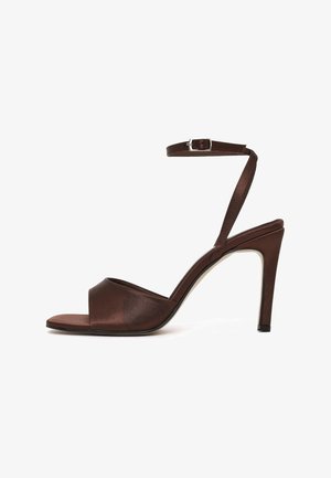 Brown high-heeled sandal with open toe, slim ankle strap with silver buckle, and stiletto heel on white background.